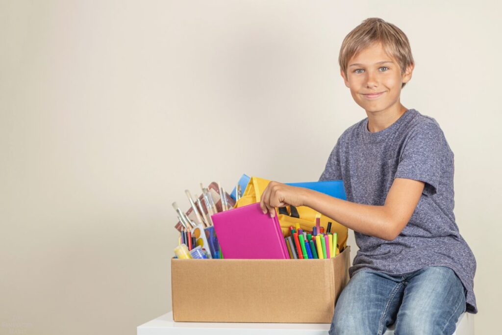 kid sitting next to box of art supplies